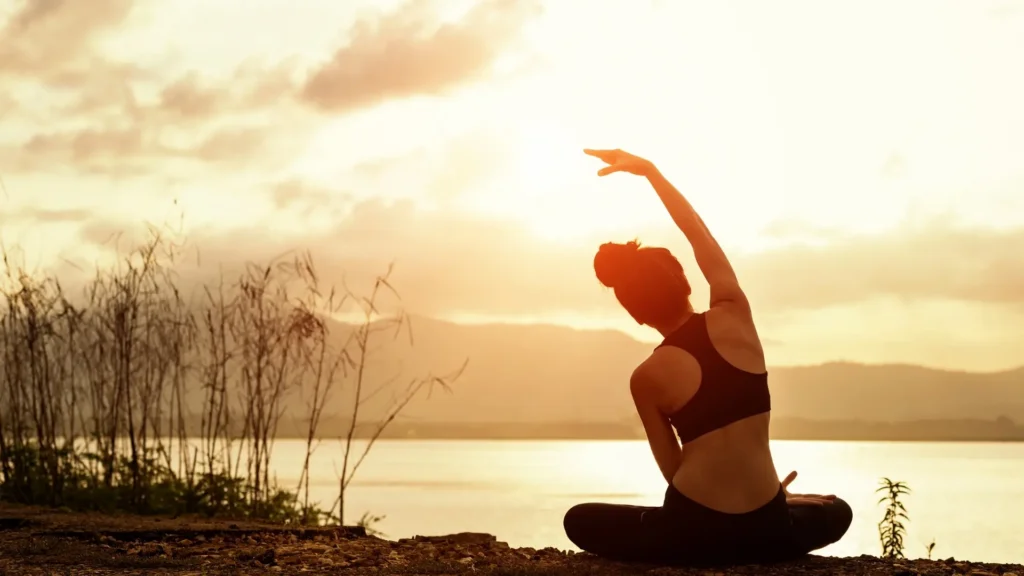 Femme qui fait du yoga devant un coucher du soleil